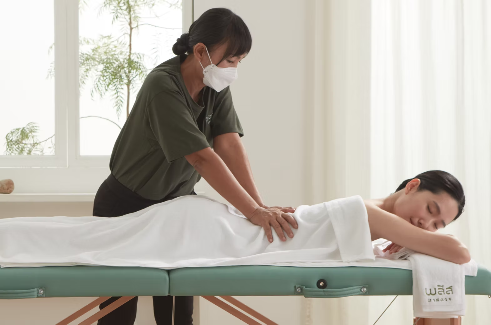 A calm therapist gives a back massage in a quiet, sunlit room
